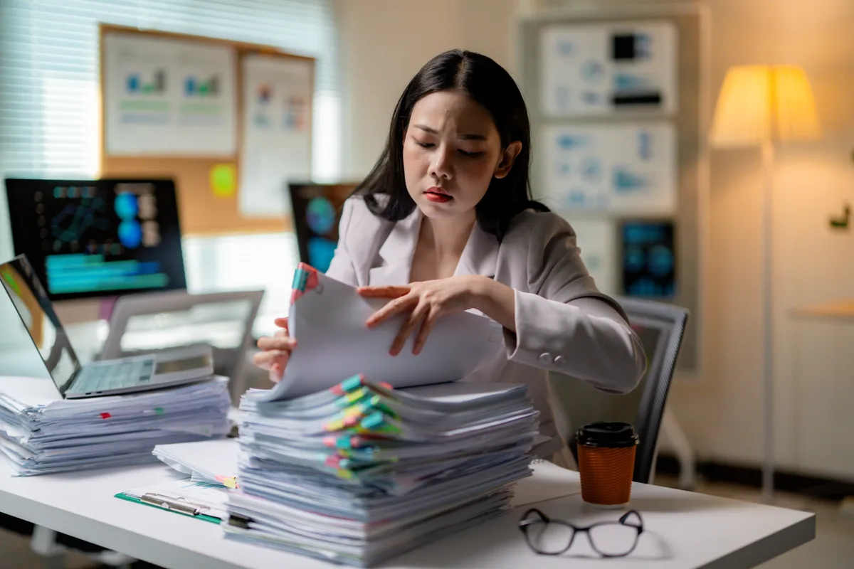 A registry officer leafing through a thick, tab-marked stack of paper filings at her desk